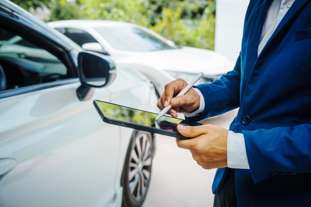 Person inspecting a vehicle with a tablet, explaining how car subscription services affect insurance coverage.