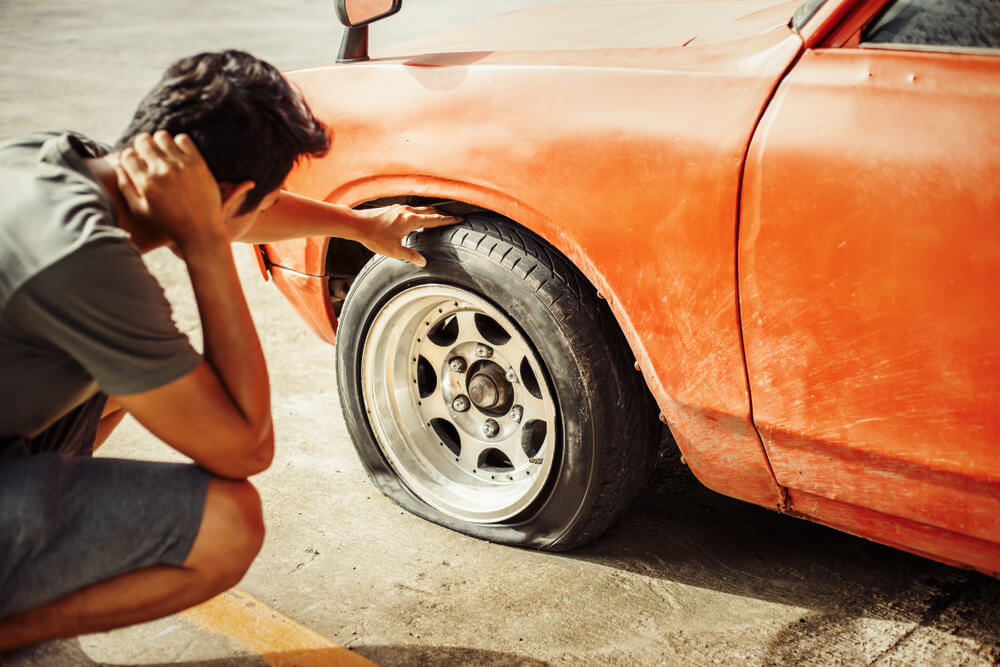 Driver checking a flat tire, one of the most common roadside breakdown causes.