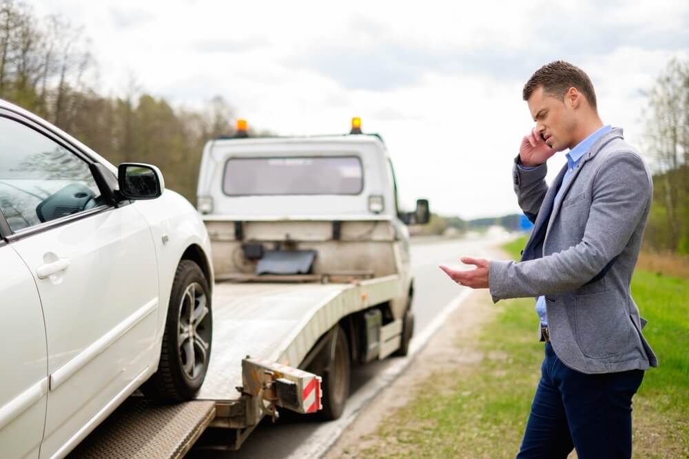 Driver calling for help beside a tow truck, illustrating insurance coverage for damage from towing.