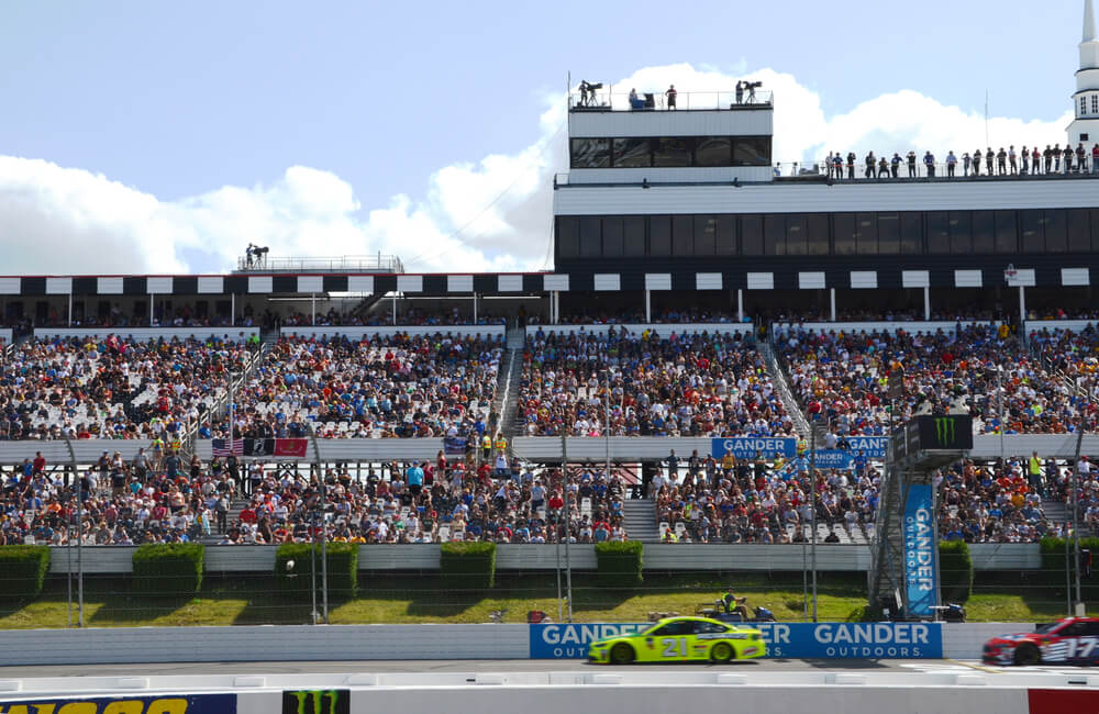 Partnership support beyond race day as NASCAR cars race past packed grandstands.