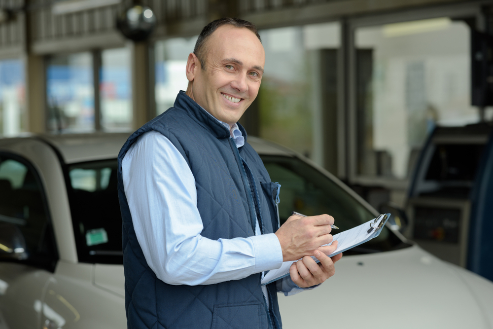 Automotive professional completing paperwork beside a vehicle for a Compliant Driver Program.