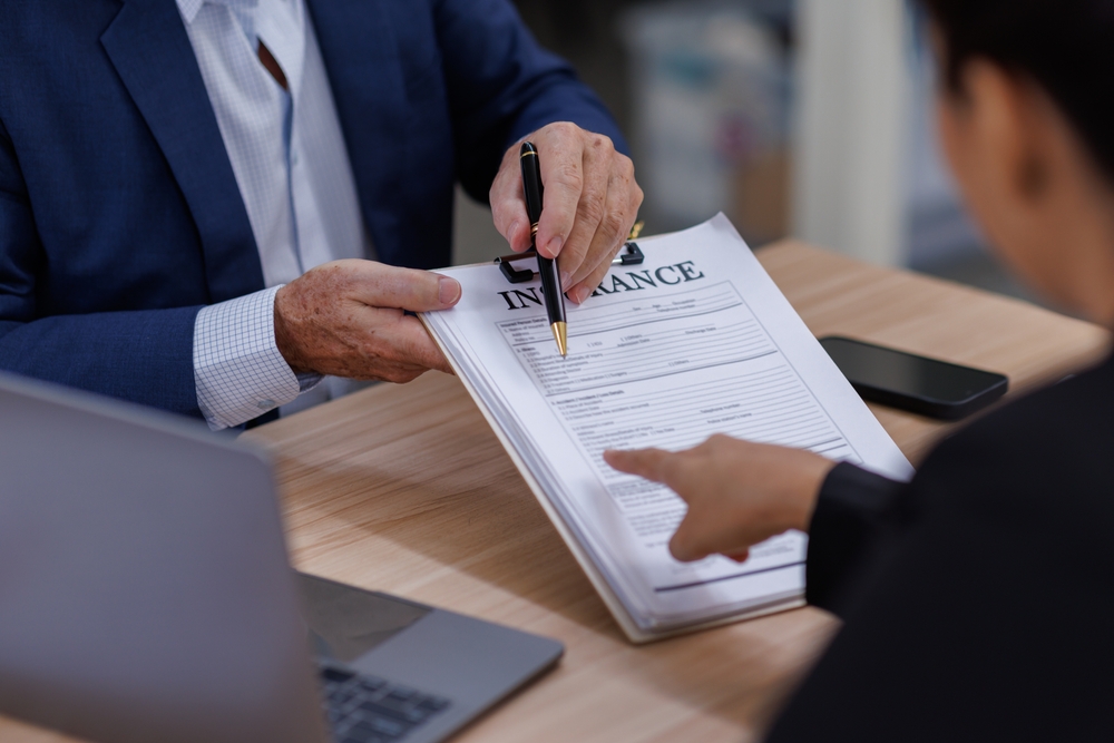 Insurance agent reviewing a car insurance policy with a customer at a desk.