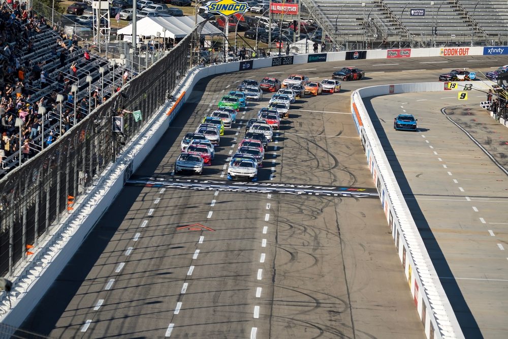 Race cars cross the start-finish line at Martinsville Speedway as spectators watch from the grandstands.