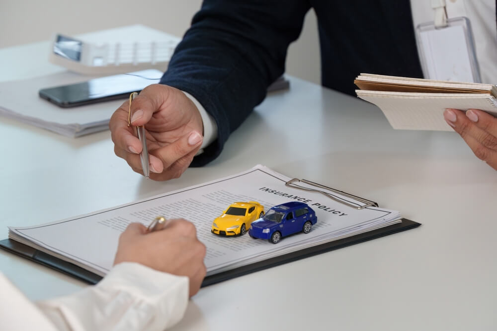 Insurance agent reviewing an auto insurance endorsement with a customer, with two miniature cars placed on an insurance policy document.