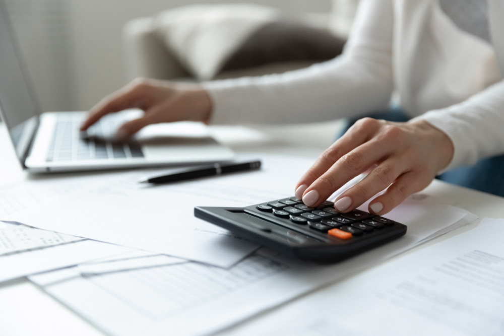 Person using a calculator and laptop to compare costs and find affordable car insurance.