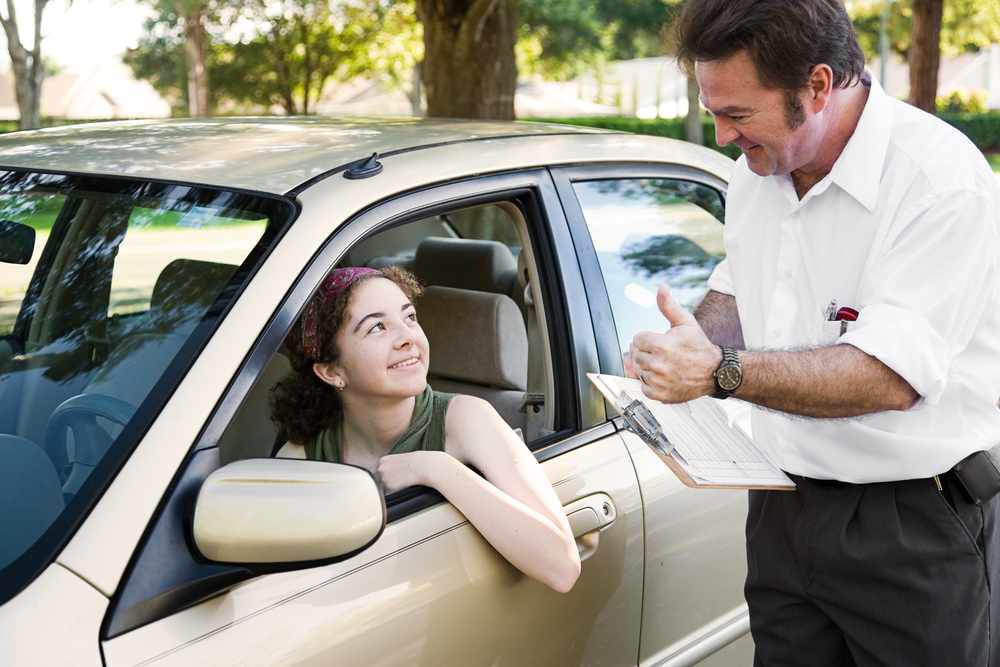 Young driver talking with a driving instructor while sitting behind the wheel of a car.