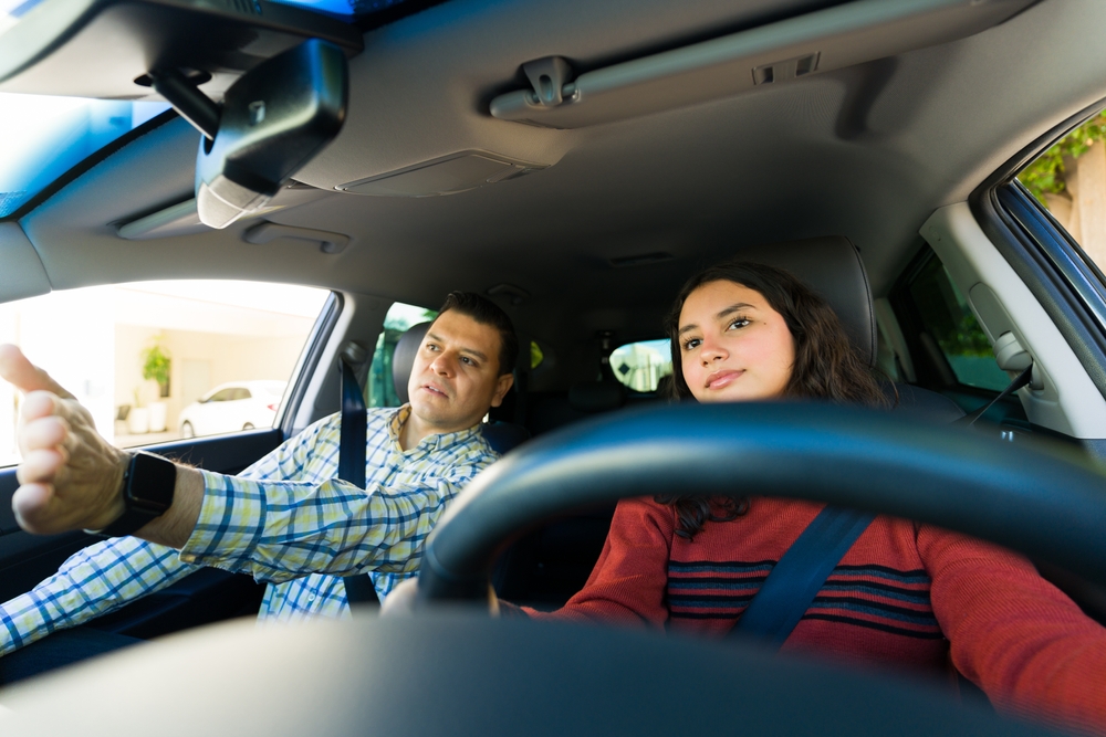 Teen driver practicing behind the wheel with an adult supervising from the passenger seat.