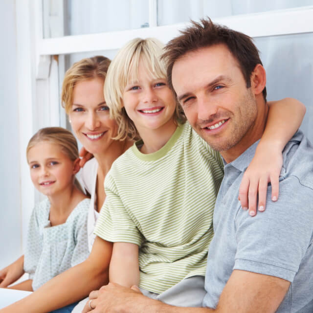 A family composed by a man, a woman, a boy and a girl smiling in front of a window.