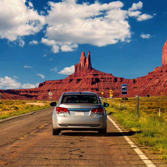 Photo of a road and cars driving toward the hills in Monument Valley, Arizona.