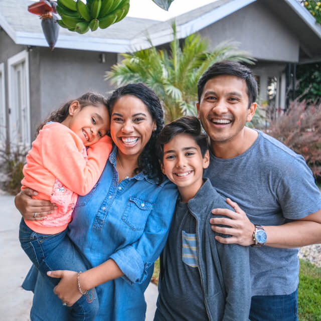 Portrait of a happy family composed by a man, a woman, a boy and a girl smiling in front of a house