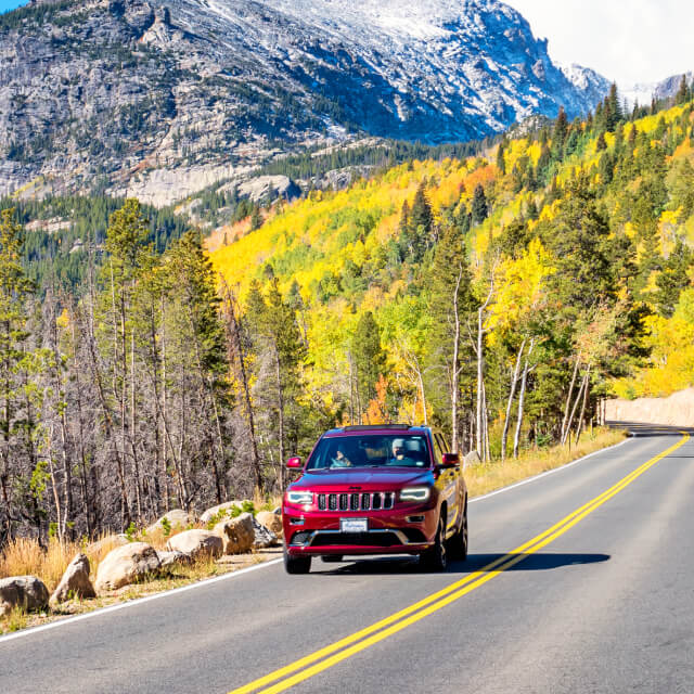 Photo of an SUV driving in Rocky Mountain National Park, Colorado with pines and mountains in the back.