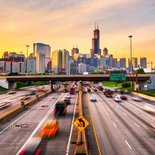 Photo of a highway with dozens of moving vehicles and the Chicago skyline in the back.