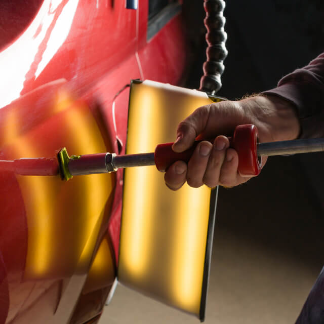 Illustrative image of a person repairing a car dent using a tool.