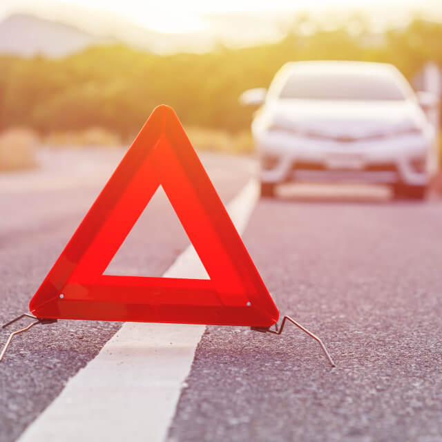 An emergency triangle stands several feet in front of a car on a country road.