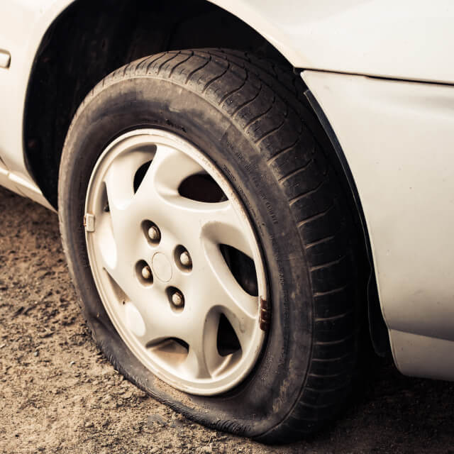 Image of the damaged flat tire of a white car with rim.