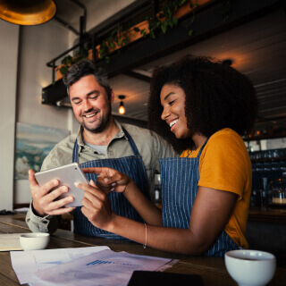 Two restaurant owners wearing a similar apron and holding a tablet.