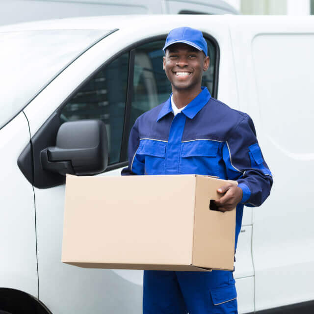 Deliveryman smiling outside a car holding a carton box.