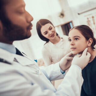 Pediatrician checking up on a girl while her mom stands on the side.