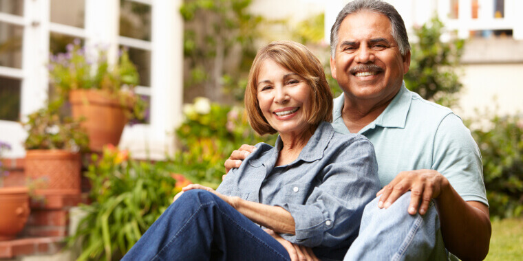 Middle age couple smiling while sitting in the backyard of a house.