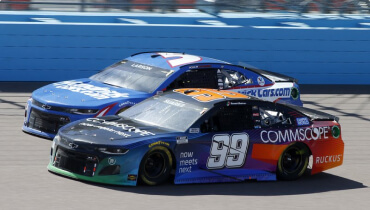 Action shot of two nascar racing cars on track with Daniel Suarez's race car with the number 99 on the door front and center