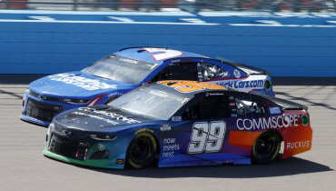Action shot of two nascar racing cars on track with Daniel Suarez's race car with the number 99 on the door front and center