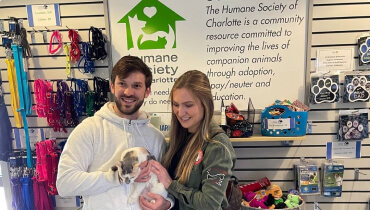 Shot of NASCAR Cup Series Driver and Xfinity Series Champion Daniel Suarez and woman smiling while holding a cat in a rescue shelter