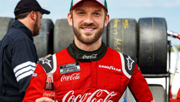 Portrait of NASCAR Cup Series Driver and Xfinity Series Champion Daniel Suarez smiling and holding a coca cola bottle
