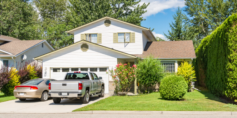 A house with a car and a truck parked in the driveway besides a garden