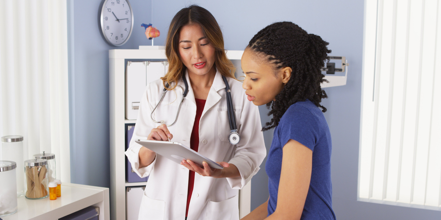 Doctor explaining diagnosis in tablet to women patient in doctors office