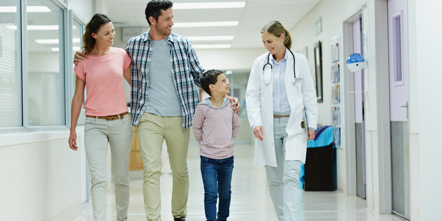 Family of man, woman and son walking with doctor female inside hospital