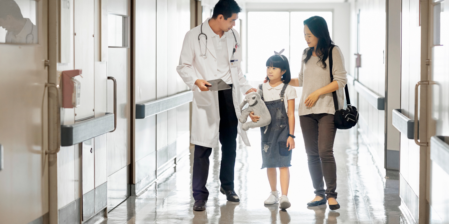 Asian American woman walking with her daughter and a doctor inside hospital