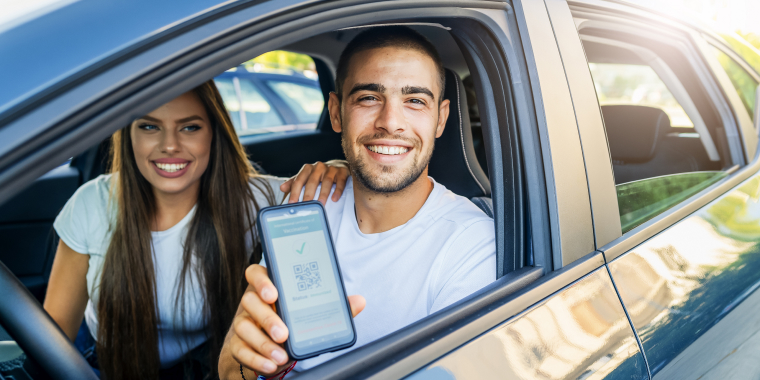 Man and woman inside their car smiling and showing phone with QR code