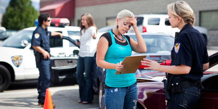 Woman getting a liability report form the police woman after a car accident and another woman speaking to a male police in the background