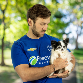Daniel Suarez in a Freeway Insurance shirt holding a dog.