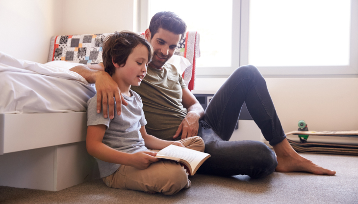 Father and son sitting on bedroom flood reading a book together