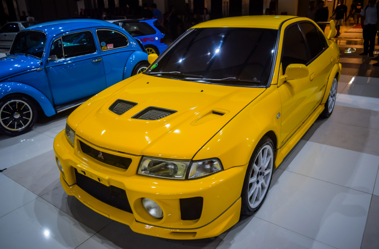Yellow Mitsubishi Lancer Evolution V in indoor car show.