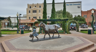 Exterior view of the Blue Bell Creameries factory in Brenham, TX, with monument depicting a girl with a cow, cheap car insurance in Texas