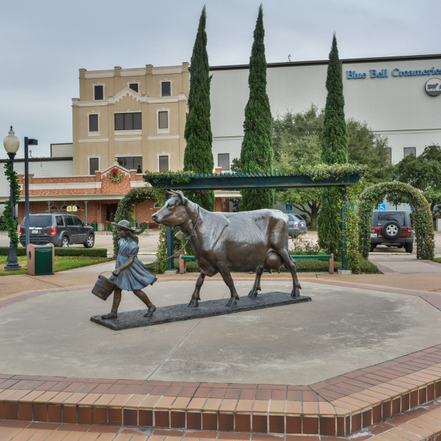 Exterior view of the Blue Bell Creameries factory in Brenham, TX, with monument depicting a girl with a cow, cheap car insurance in Texas