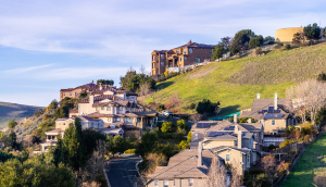 Residential neighborhood with multilevel single family homes, built on a hill; water tank visible on top of the hill in Hayward, East San Francisco Bay Area: Cheap car insurance in California.