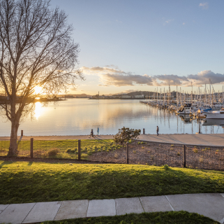 Bay water view of sunset in Richmond, California with a harbor, boats, and people walking and biking on sidewalks and trails: Cheap car insurance in The Golden State.