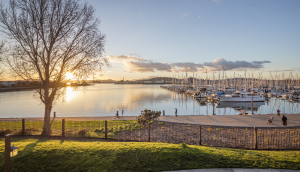 Bay water view of sunset in Richmond, California with a harbor, boats, and people walking and biking on sidewalks and trails: Cheap car insurance in The Golden State.