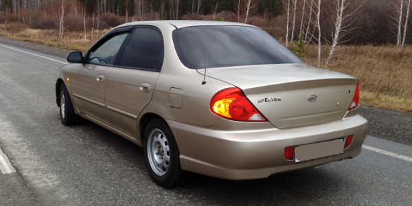 Kia Spectra car is located on the highway against the background of a cloudy autumn sky - cheap car insurance.