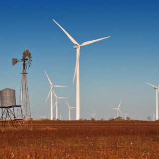A vintage windmill with modern wind turbines in the background. Located in a cotton field in Snyder, TX