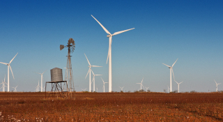 A vintage windmill with modern wind turbines in the background. Located in a cotton field in Snyder, TX