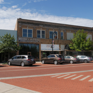 A brick-paved street with old buildings and cars parked in the roadside in Sulphur Springs, Texas: cheap car insurance in Texas.