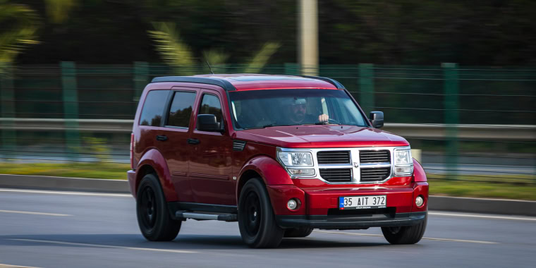 Red Dodge Nitro driving quickly on a sunny street with palm trees in Alanya, Turkey.