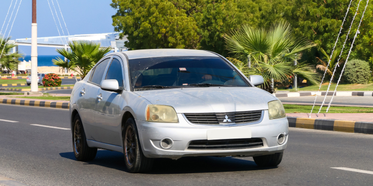 Grey Mitsubishi Galant driving down highway on summer day.