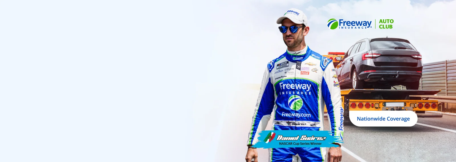 NASCAR driver Daniel Suarez wearing a Freeway Insurance suit standing next to a tow truck.