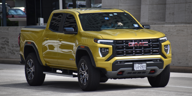 A portrait of a yellow metallic-colored GMC Canyon pickup truck cruising in the downtown financial district of Houston, Texas – cheap car insurance.