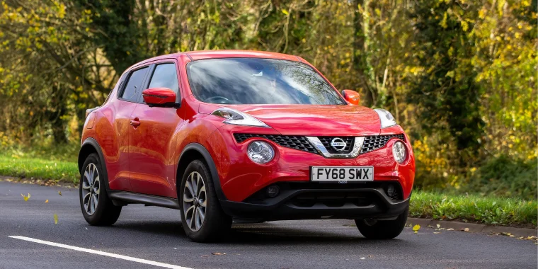 Red Nissan Juke advancing on a tree-lined road in Milton Keynes, Bucks, UK – cheap car insurance